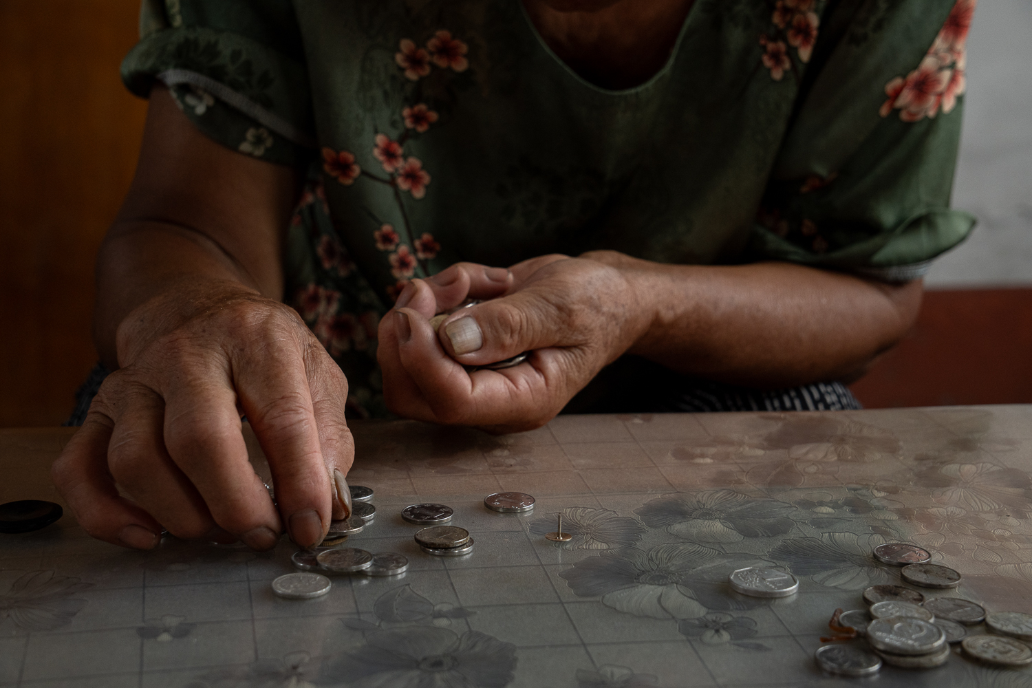 A close view of a woman counting coins on a patterned tabletop.