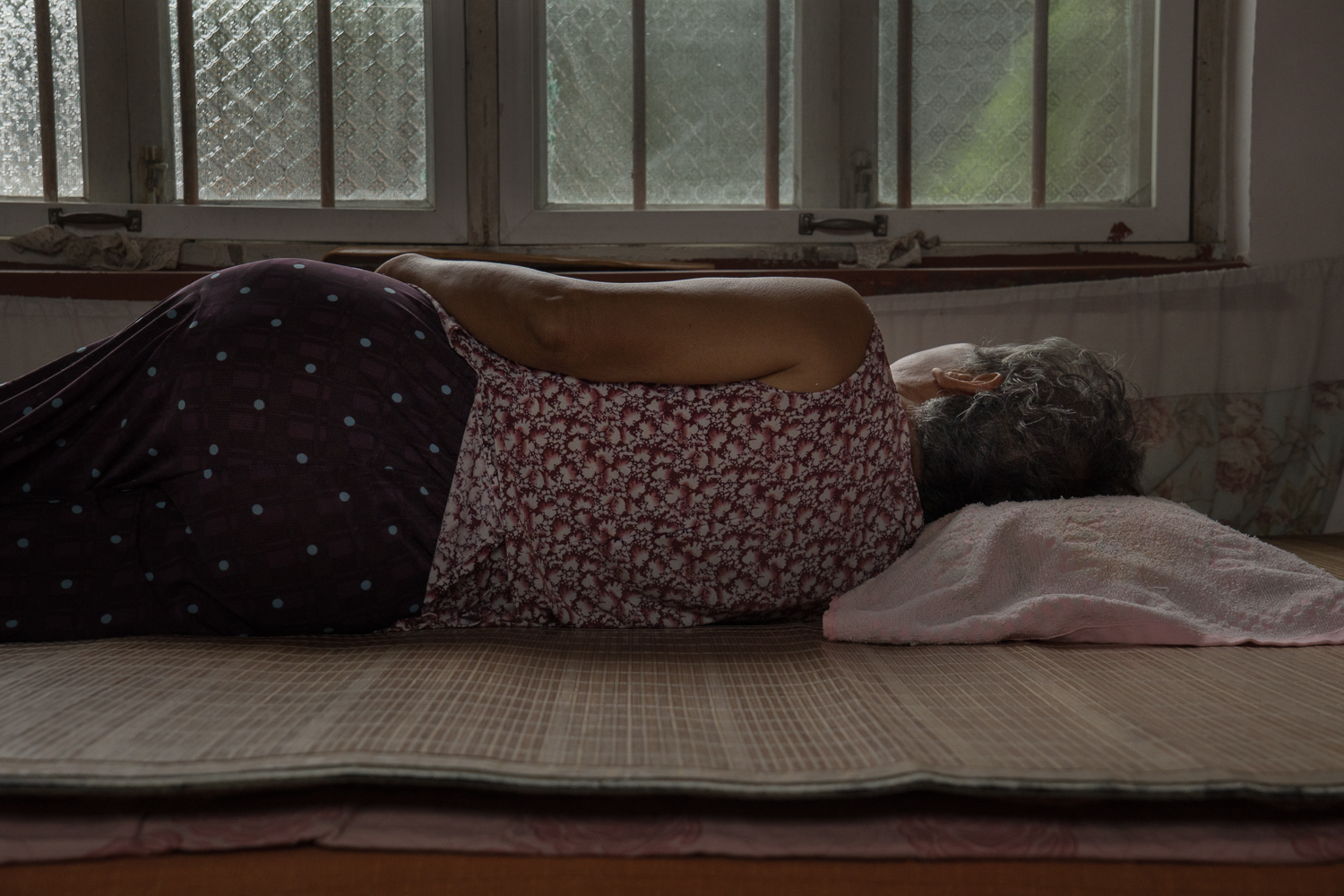 A woman resting on her side on a woven mat beside a window.
